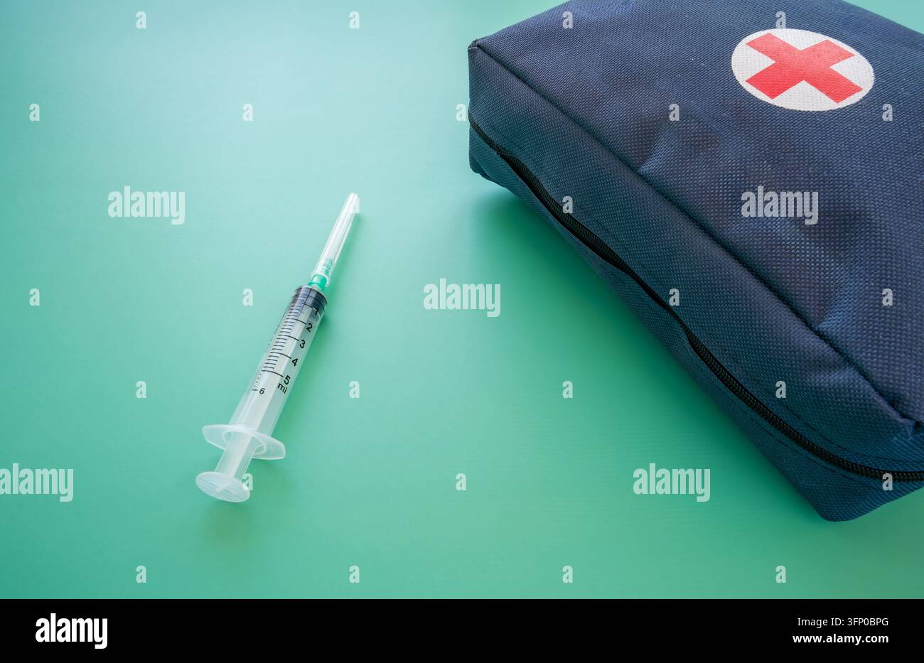 Blauer Erste-Hilfe-Kasten mit rotem Kreuz und graduierten Spritzen, angeordnet auf einem türkisfarbenen Hintergrund, zeigt medizinische Ausrüstung und transparente Kunststoffdetails Stockfoto
