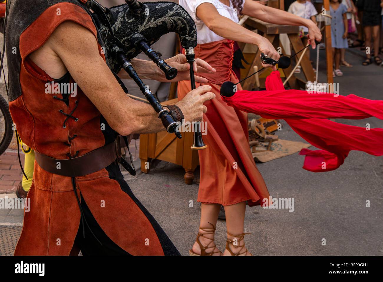 Straßenmusiker spielt traditionelle Dudelsäcke, während er in einem historischen mittelalterlichen Kostüm gekleidet ist. Die Szene ist lebhaft, mit anderen Darstellern und Publikumsmitgliedern Stockfoto