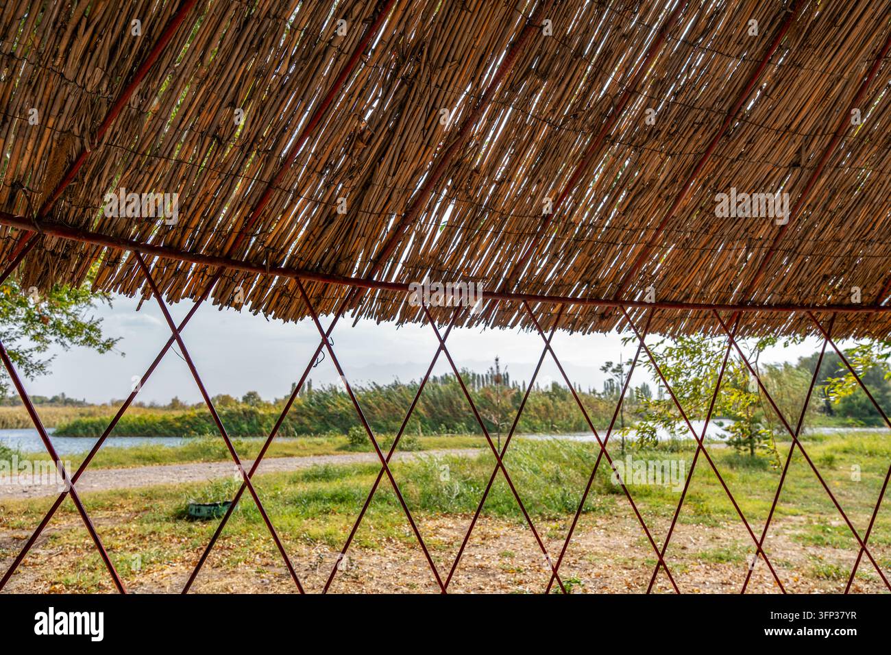 Innenansicht einer umweltfreundlichen Hütte mit einem getrockneten Schilfdach und geometrischem Rahmen, die eine malerische Landschaft mit Wasser und grünen Feldern zeigt Stockfoto