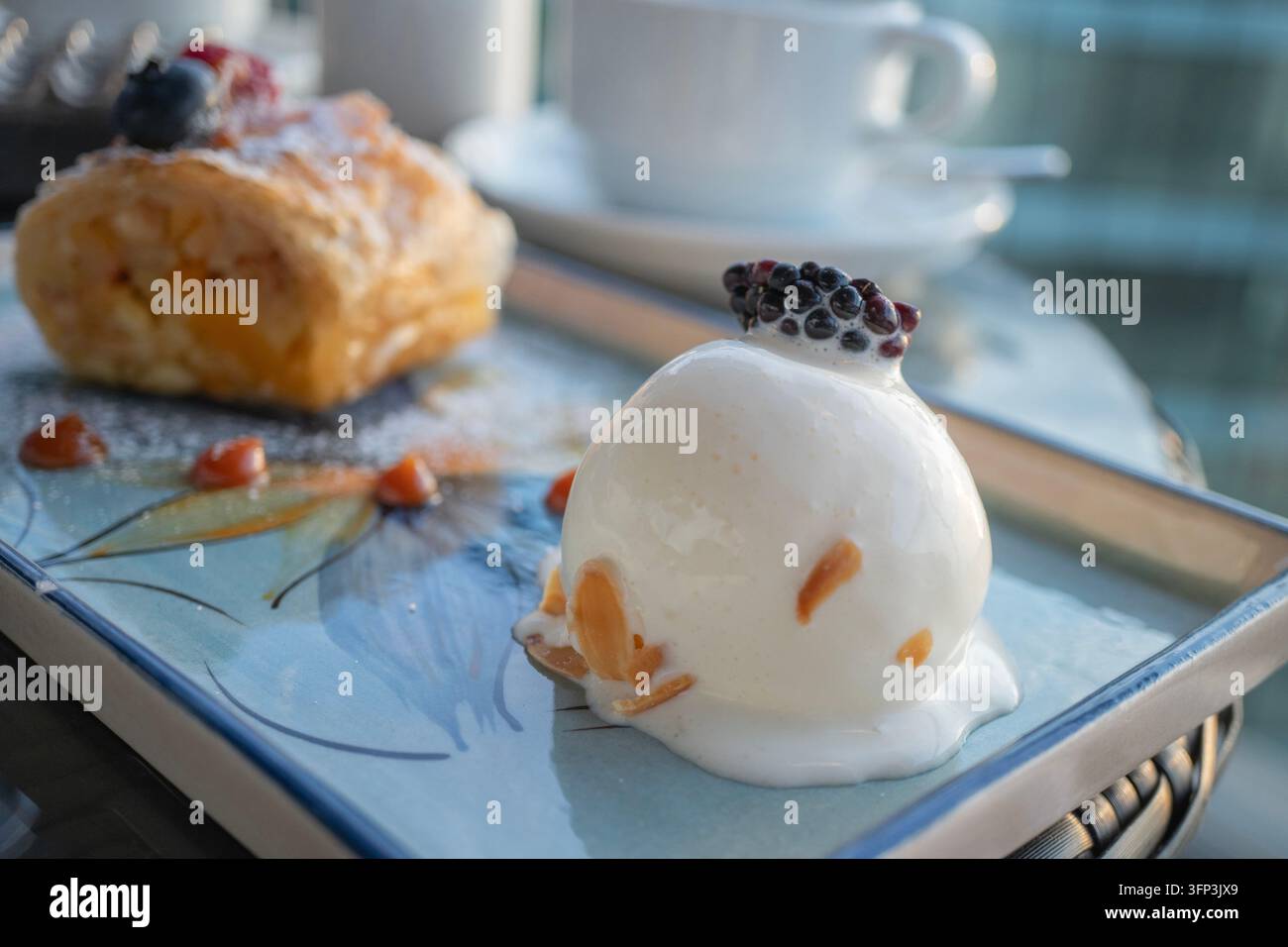 Ein weiß glasierter Mousse-Kuppelkuchen, verziert mit Beeren und Mandeln, neben einem goldenen, blättrigen Blätterteigrollen-Dessert, elegante süße Leckereien auf einem de Stockfoto