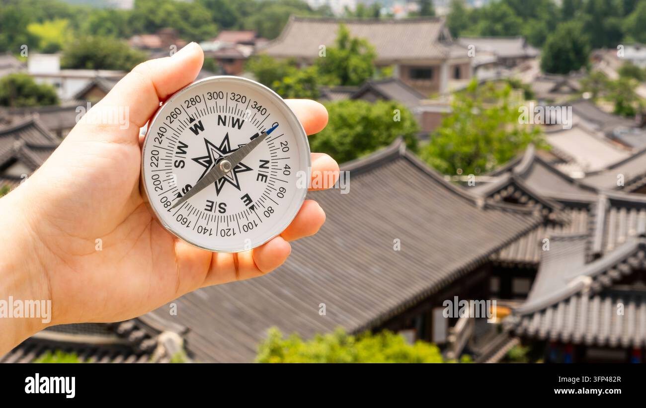 Runder Kompass in der Hand vor dem Hintergrund traditioneller koreanischer Häuser namens Hanok im Jeonju Hanok Village, Südkorea Stockfoto