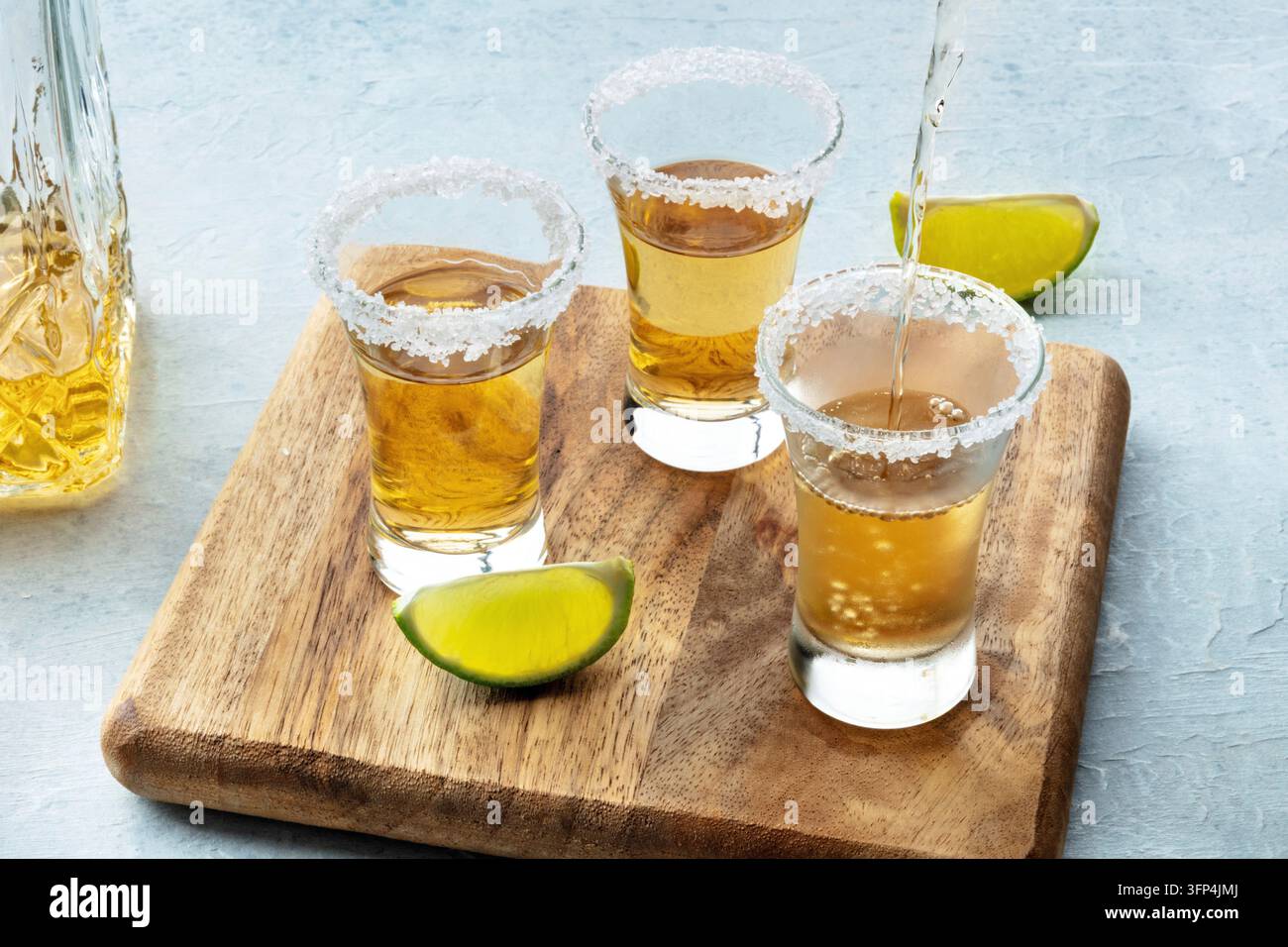 Tequila in ein Glas mit gesalzenem Rand und Limettenscheiben auf Schiefergrund gegossen Stockfoto