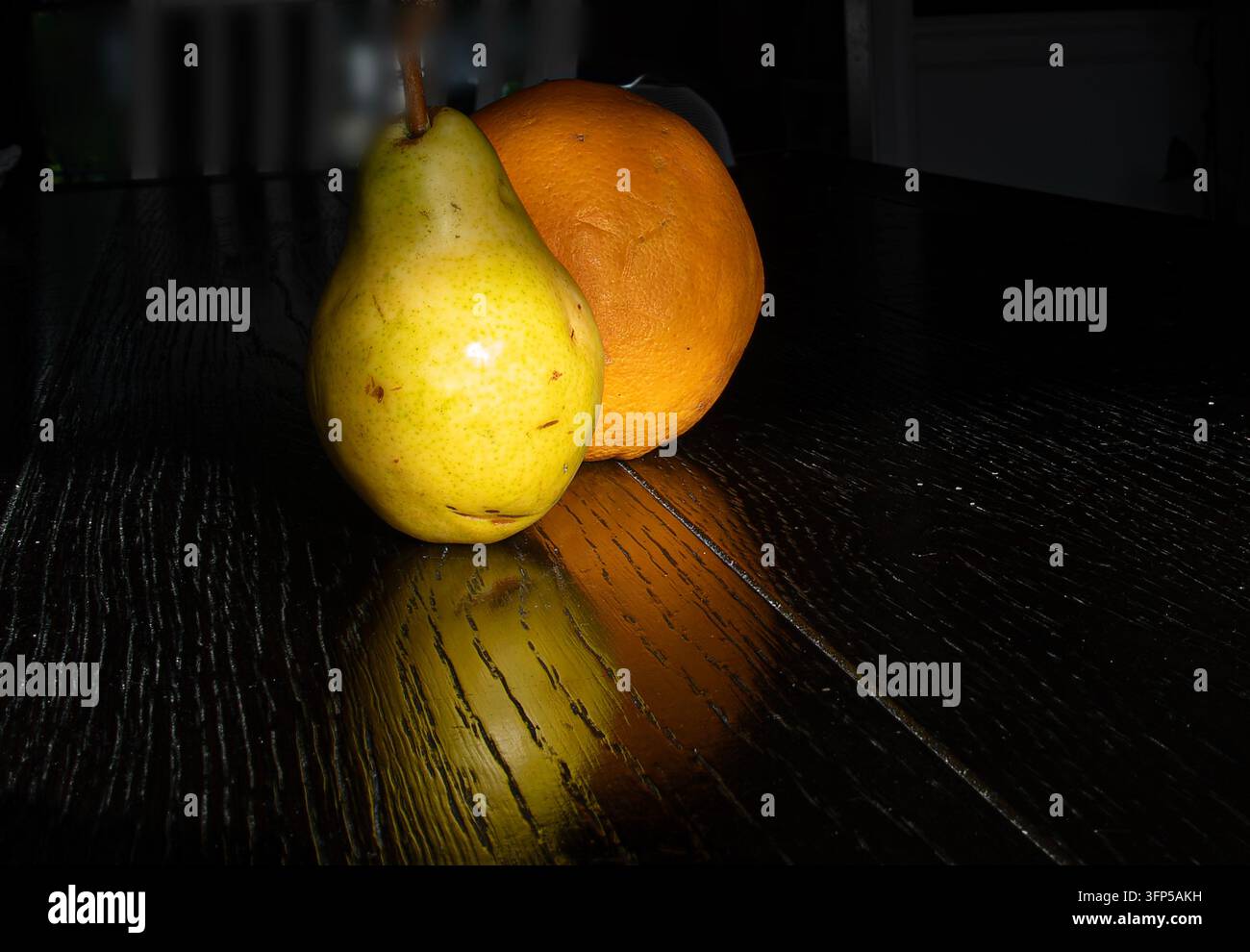 Eine frische grün-gelbe Birne ruht neben einer strukturierten Orange auf einem dunklen, polierten Holztisch. Stockfoto