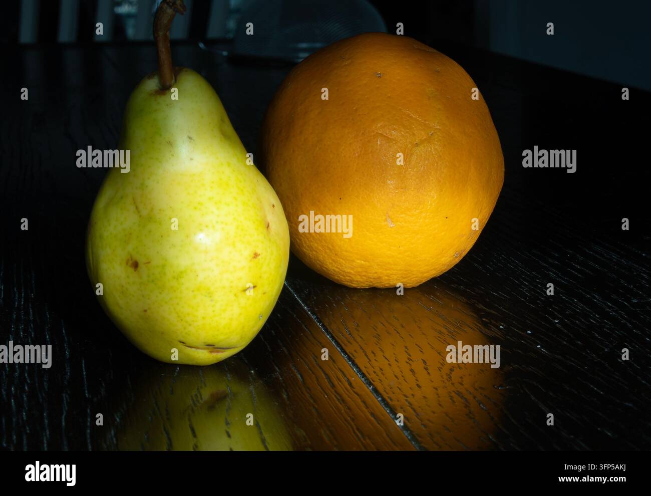 Eine frische grün-gelbe Birne ruht neben einer strukturierten Orange auf einem dunklen, polierten Holztisch. Stockfoto