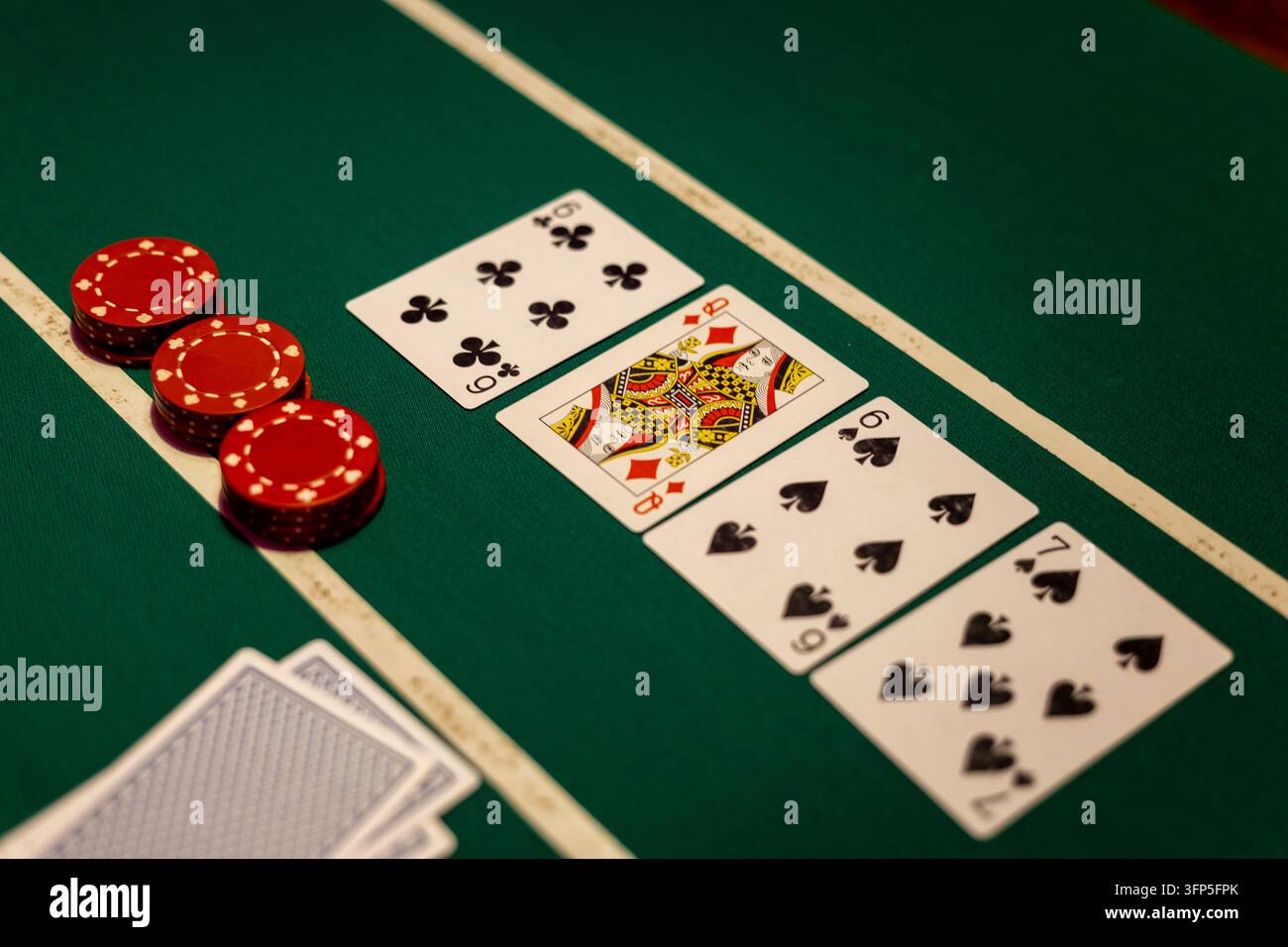 Grünes Poker-Felt zeigt vier offene Spielkarten in einer Reihe neben Stapeln roter Einsatzmarken. Brett zeigt Herzbube sechs, Karo-Dame, Pik sechs. Stockfoto
