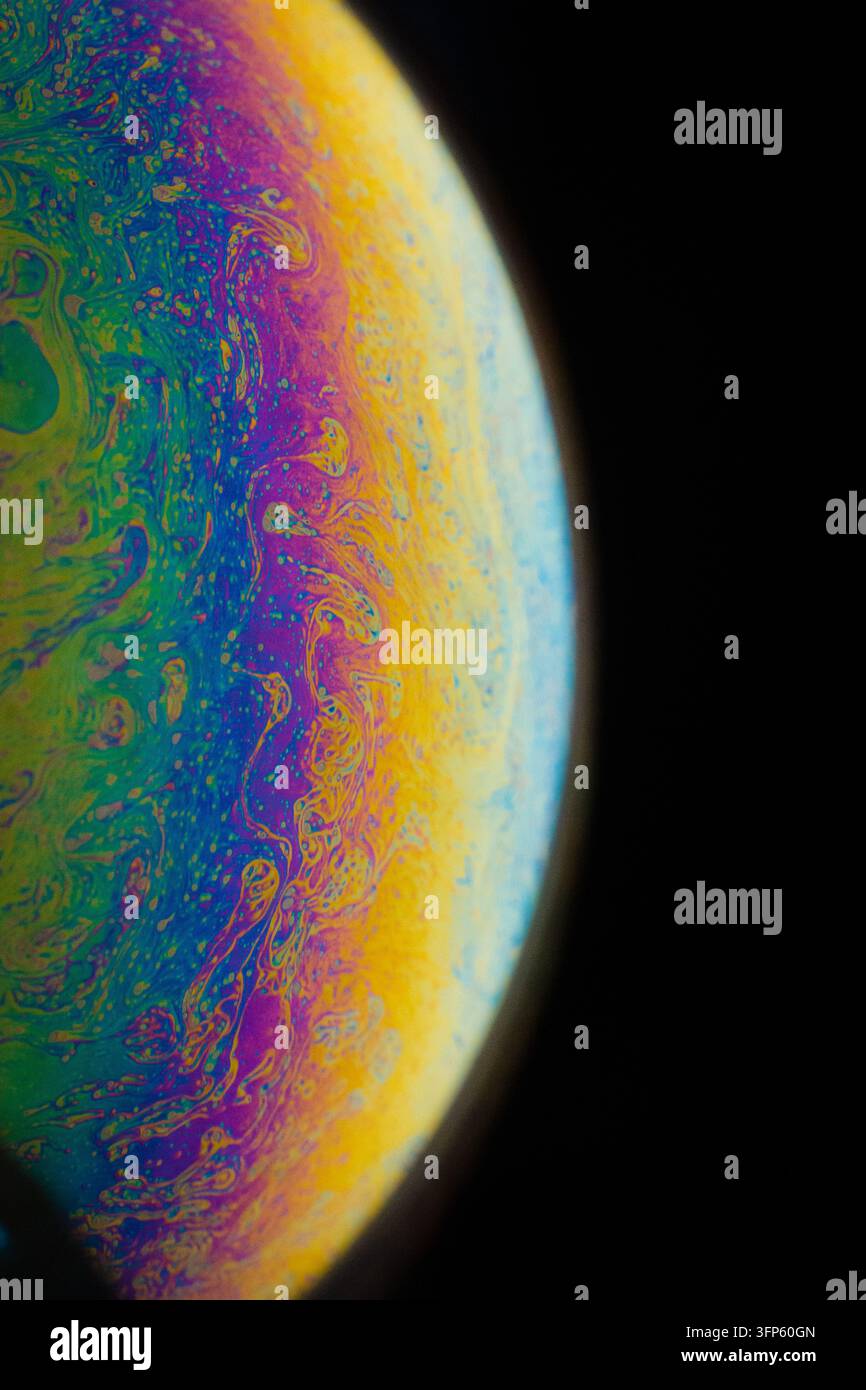 Makro-Nahaufnahme einer irisierenden Seifenblasenoberfläche, die lebendige kosmische Regenbogenfarben vor dunklem Hintergrund zeigt Stockfoto