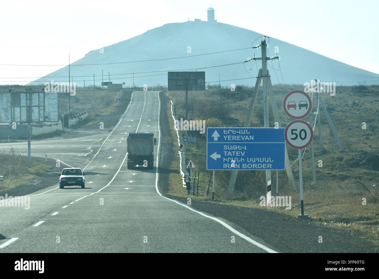 Ein zweisprachiges blaues Autobahnschild weist den Verkehr in Richtung Jerewan, Tatew und die iranische Grenze entlang der Haupttransitzstraße in der Provinz Syunik, Armenien. Stockfoto
