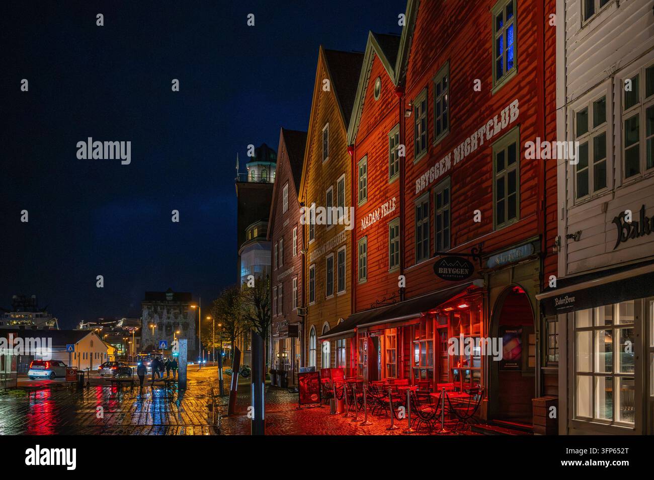 Bryggen, Bergen, Norwegen, Straße bei Nacht gesäumt von bunten Holzgebäuden, in einem davon ist der Bryggen Nachtclub sichtbar, beleuchtet von roten Lichtern Stockfoto