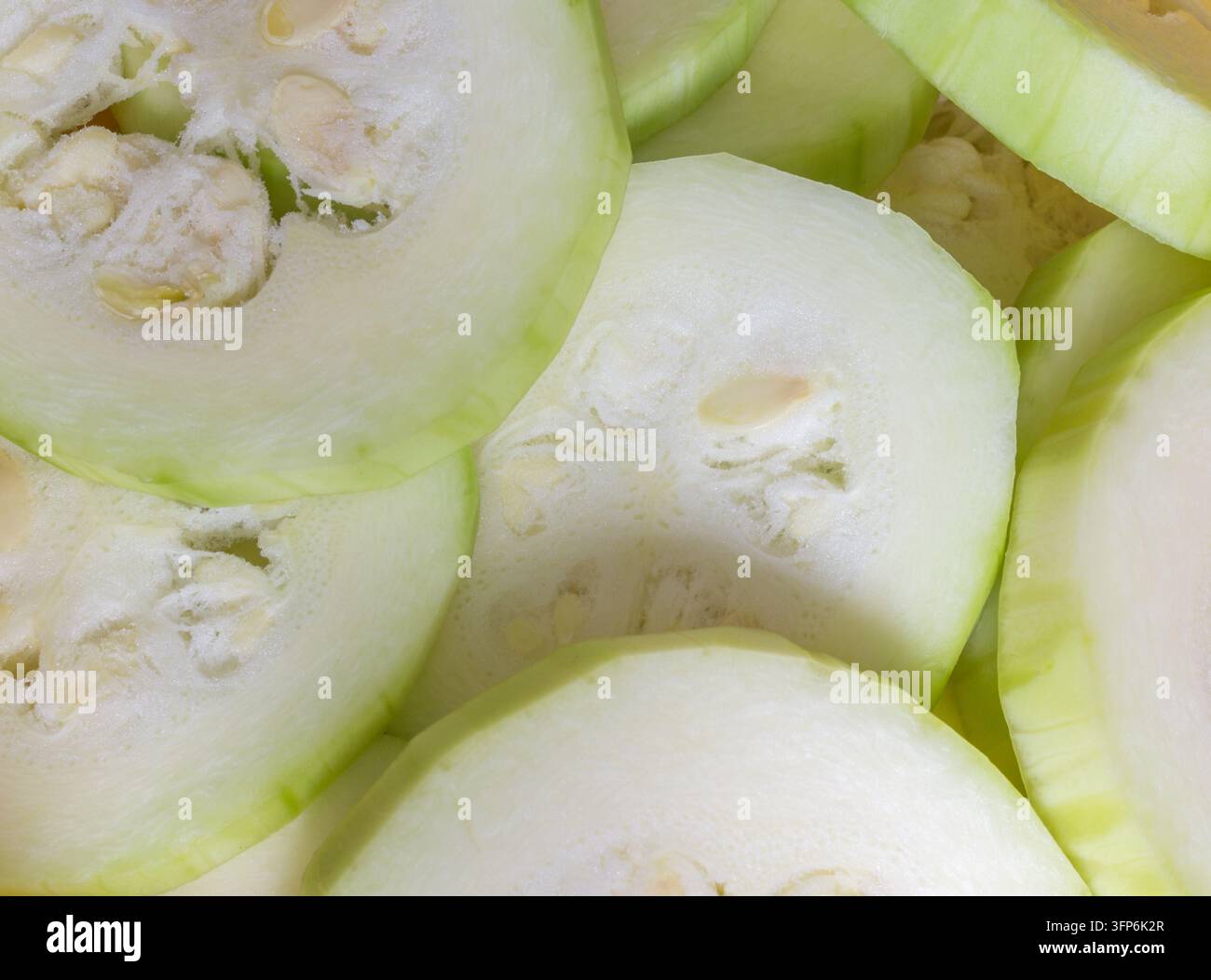 Nahaufnahme von frisch geschnittenem Zucchini, zeigt hellgrüne Schale, weiches weißes Fleisch und sichtbare Samen in runden Gemusescheiben Stockfoto