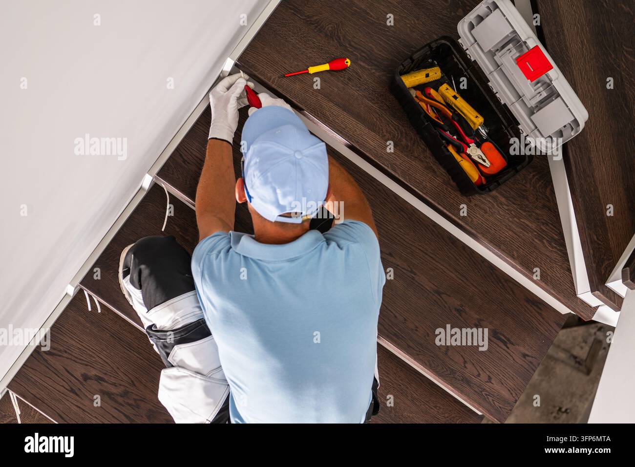 Oberblick auf einen Elektriker, der neben hölzernen Treppenstufen an der Verkabelung arbeitet, mit einem offenen Werkzeugkasten und isolierten Werkzeugen auf den Stufen. Stockfoto