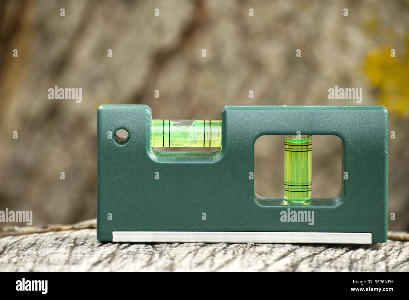 Grüne Wasserwaage auf einer strukturierten Holzoberfläche mit horizontalen und vertikalen Luftpolsterröhrchen zur präzisen Nivellierung in Zimmerei, Bauwesen, Stockfoto