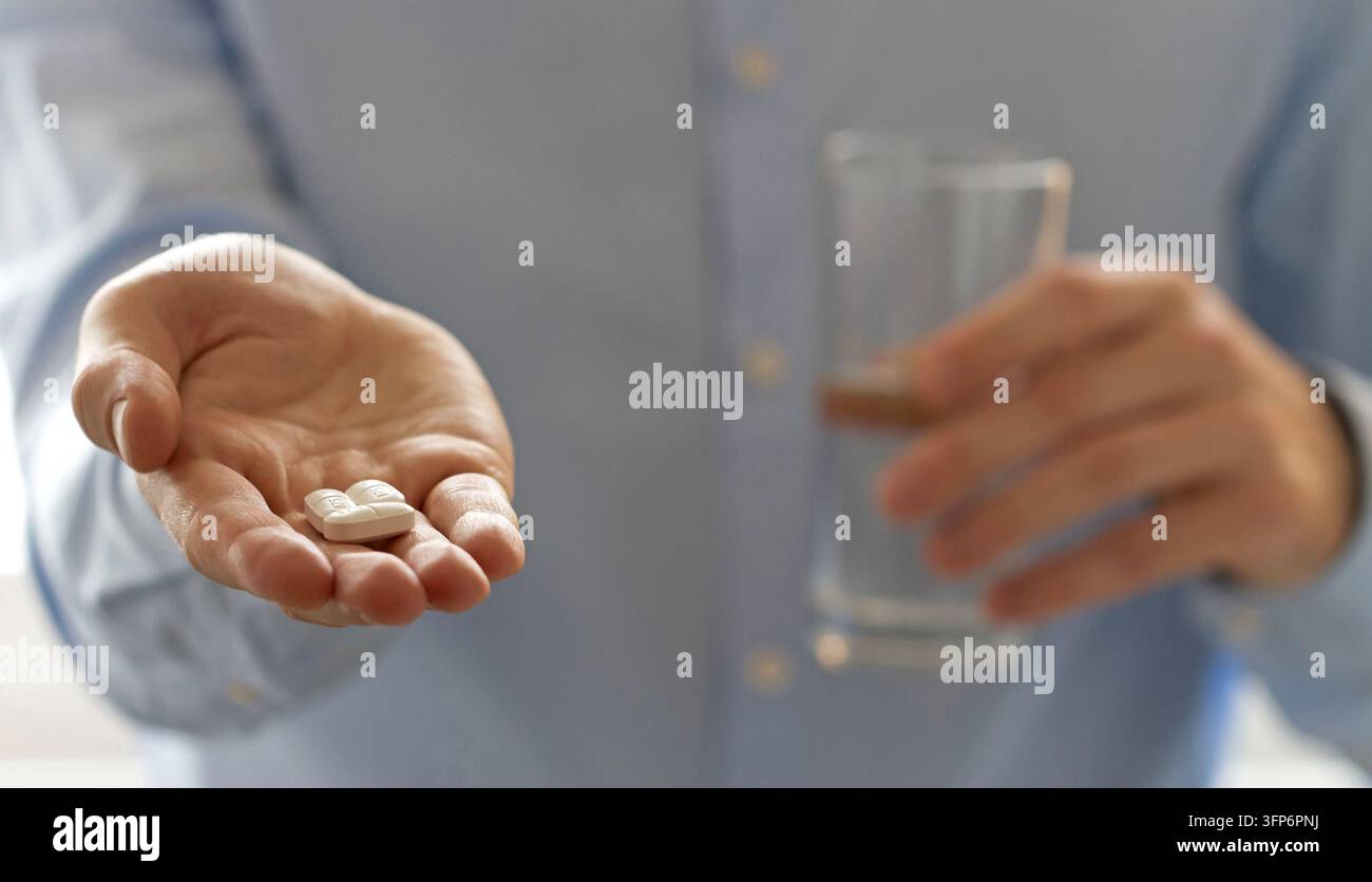 Nahaufnahme einer Person, die weiße Tabletten in der offenen Hand anbietet, während sie ein Glas Wasser hält, was die Einnahme von Medikamenten, Behandlung und tägliche Gesundheitsvorsorge vermittelt Stockfoto