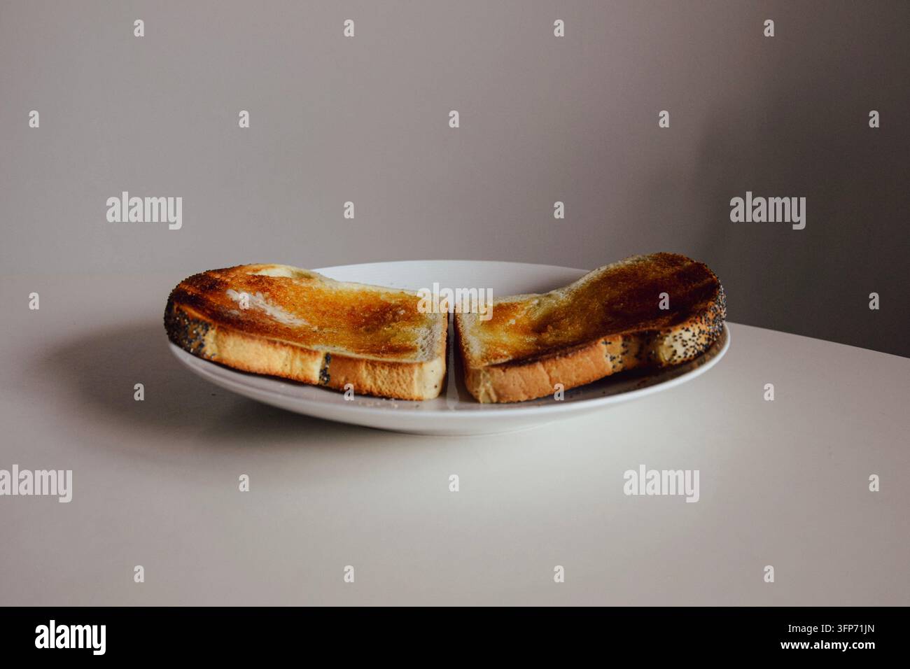 Zwei Scheiben goldbrauner Toast mit Butter und Mohn auf einem weißen Teller Stockfoto