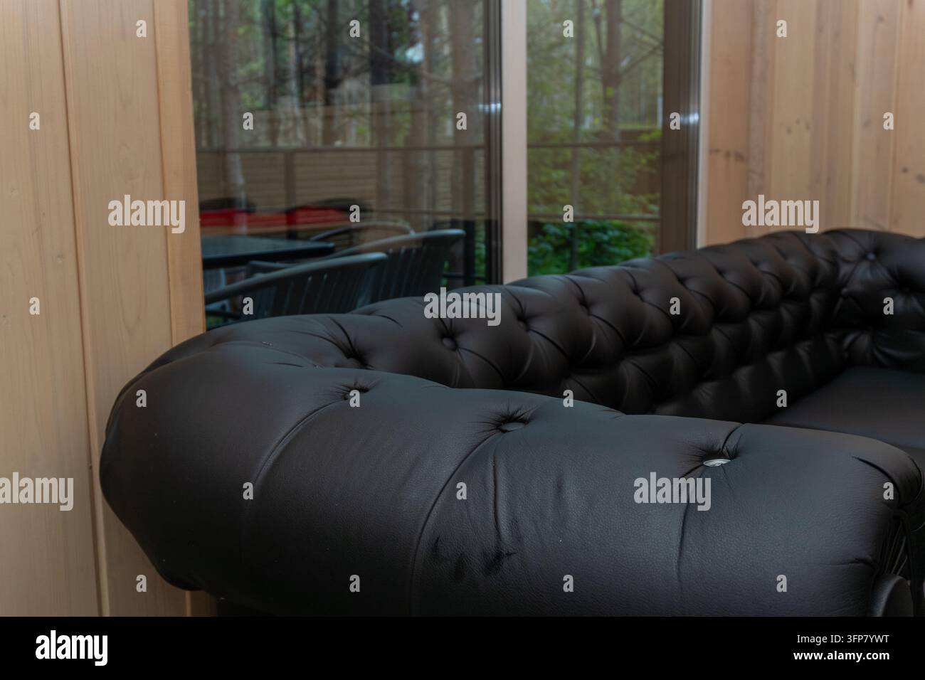 Schwarzes Chesterfield-Sofa aus Leder in einem Raum mit Panoramafenster Stockfoto
