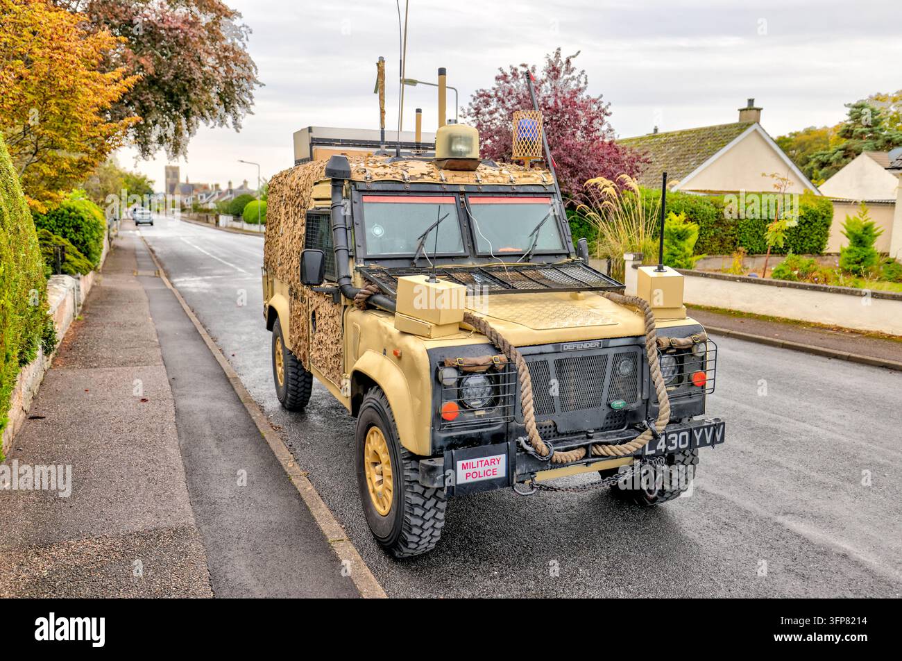 Ein mit Tarnfarbe gestrichener Land Rover Defender, ausgestattet mit einem Dachträger, Antennen und Expeditionzubehör, parkt entlang einer Wohnstraße in den Scottis Stockfoto