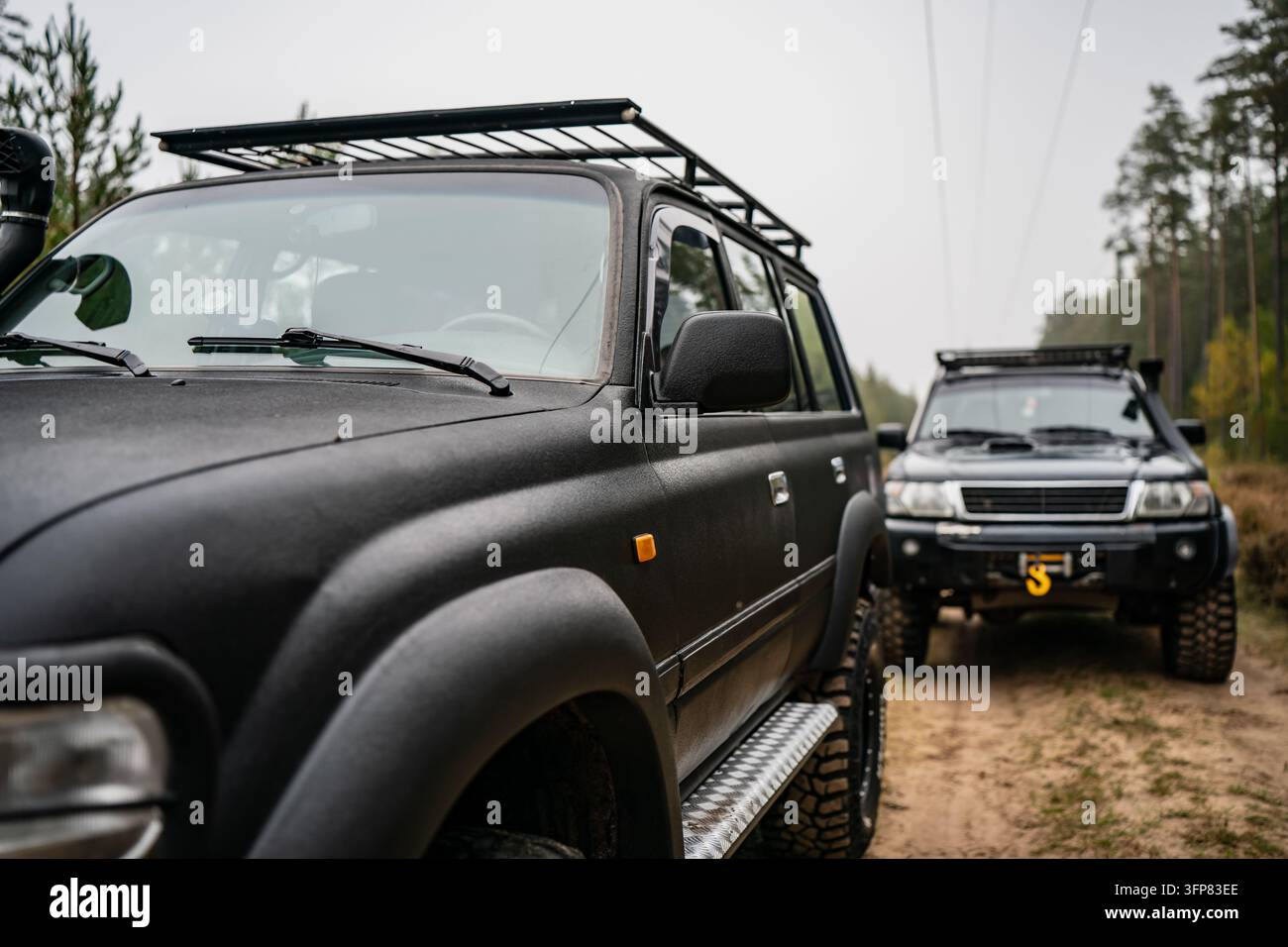 Paar von Geländewagen-SUVs, die entlang eines sandigen Waldweges mit Dachträgern und Bergungsausrüstung geparkt sind, repräsentieren Freizeitgruppenreisen und Fahrzeug Stockfoto