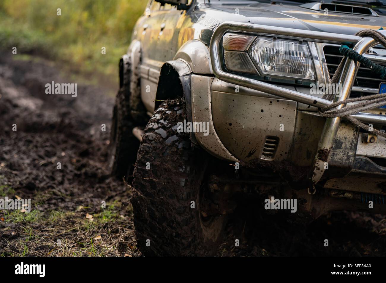 Geländewagen mit schlammbedecktem Reifen, vorderer Bullenfänger und angebrachten Seilen auf einem holprigen Waldweg, zeigt Zugausrüstung für Freizeit-4x4-J Stockfoto