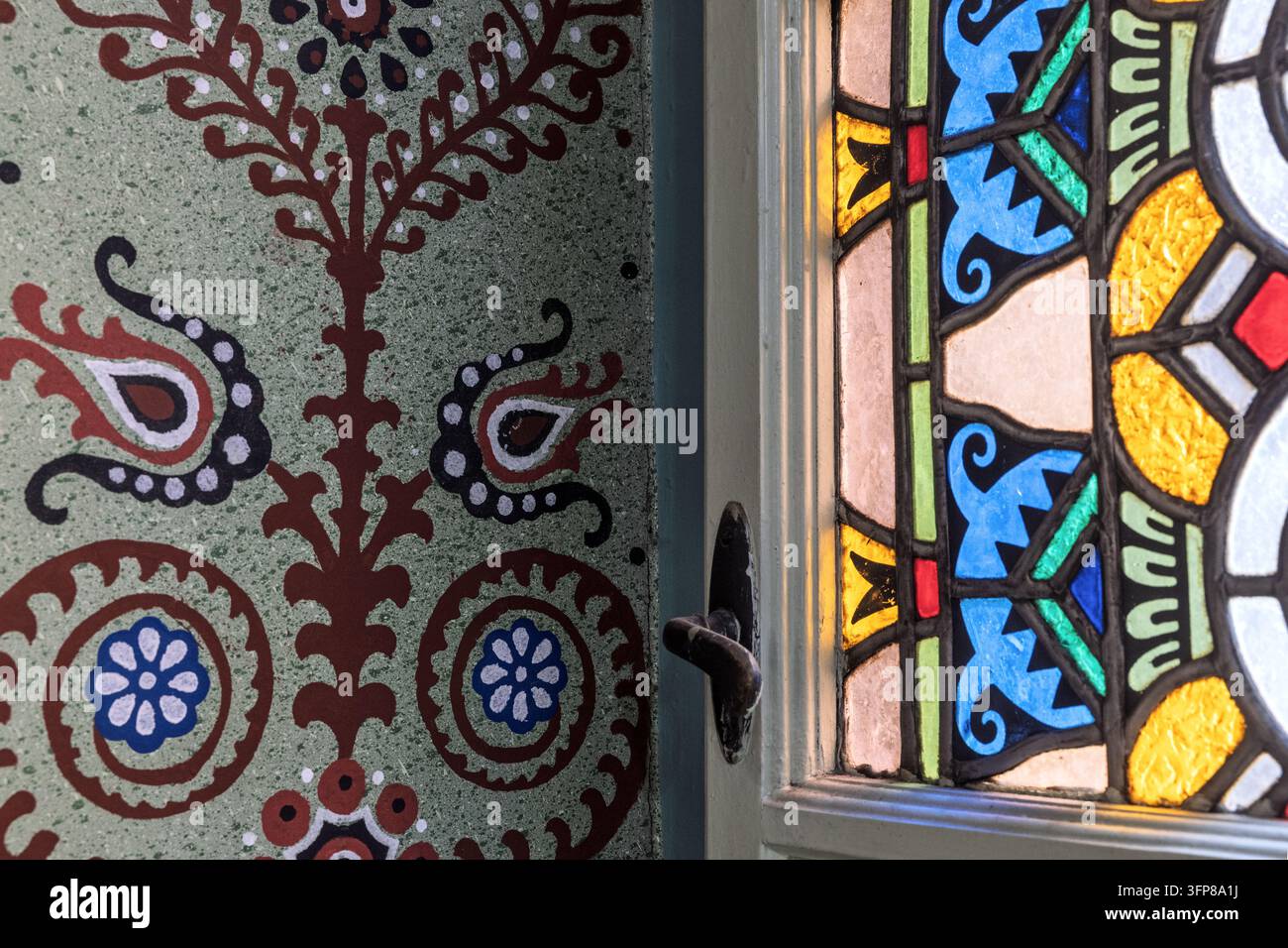 Nahaufnahme einer handbemalten Wand mit Paisleymustern neben einem farbenfrohen Buntglasfenster, Rathaus von Subotica, Subotica, Serbien Stockfoto