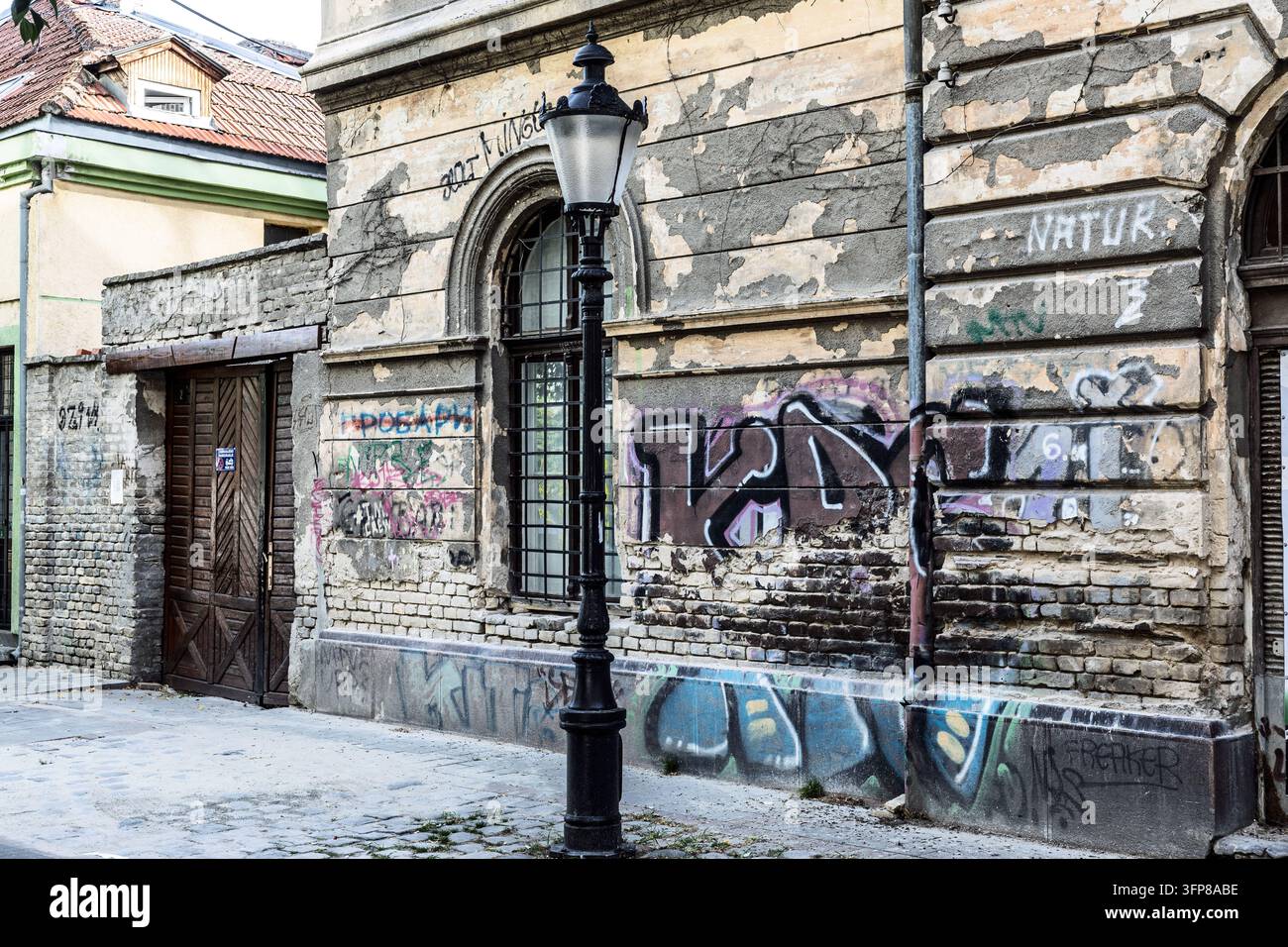 Ein altes städtisches Gebäude mit verwitterten Wänden, geschichteten Graffiti und einer klassischen Straßenlaterne, Subotica, Serbien Stockfoto