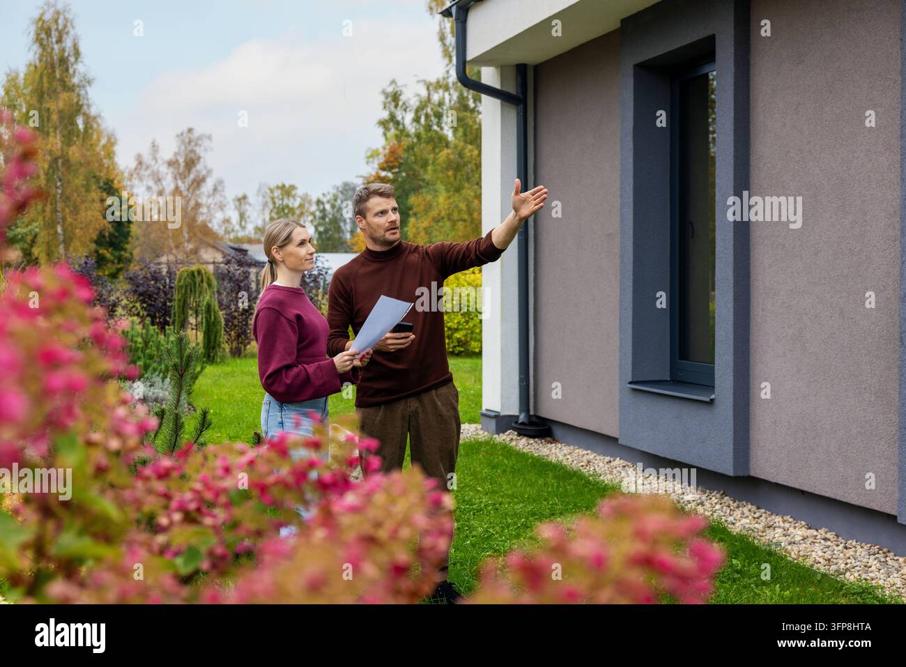 Paar betrachtet modernes neues Haus mit gestaltetem Garten. Immobilienbesichtigung vor dem Kauf. Immobilienmarkt Stockfoto