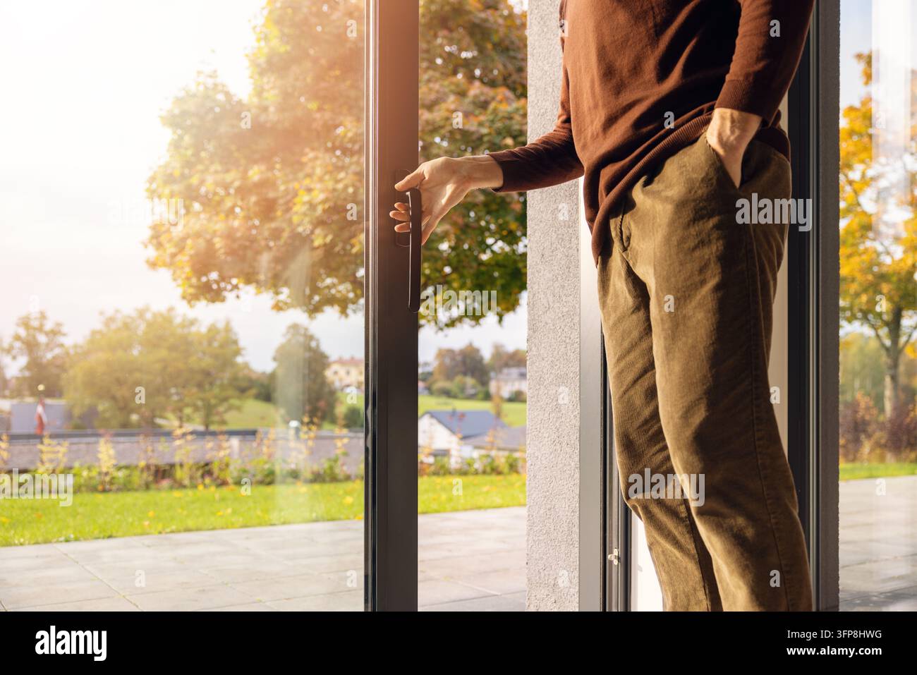 Mann öffnet große Aluminium-Schiebetür aus Glas zur Gartenterrasse Stockfoto