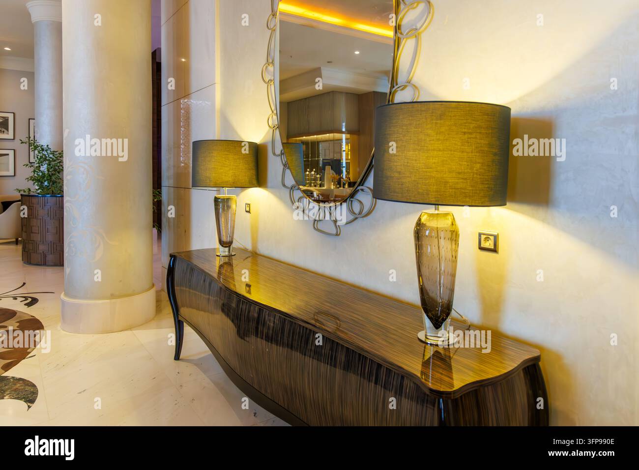 Horizontale Nahaufnahme eines gehobenen Boutique-Hotel-Flurs mit einer polierten Holzkonsole, einem Design-Spiegel und stilvollen Tischlampen. Stockfoto