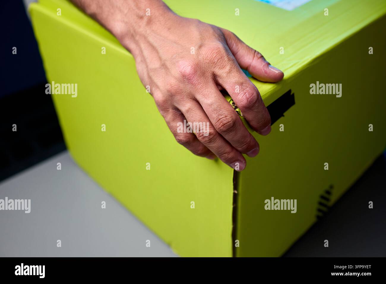 Hände, die eine hellgelbe Paketbox auf einer Tischplatte öffnen Stockfoto