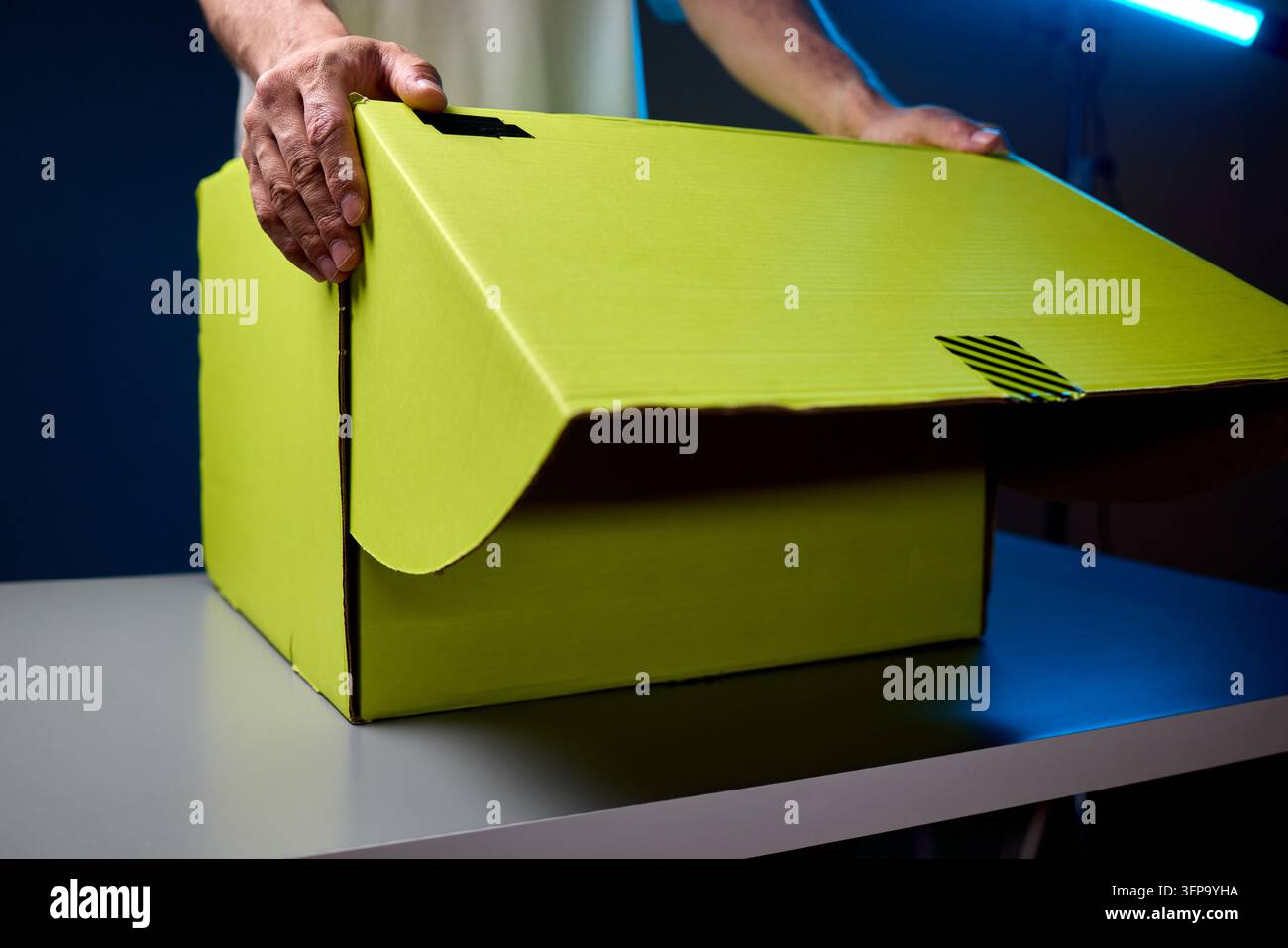 Hände, die eine hellgelbe Paketbox auf einer Tischplatte öffnen Stockfoto