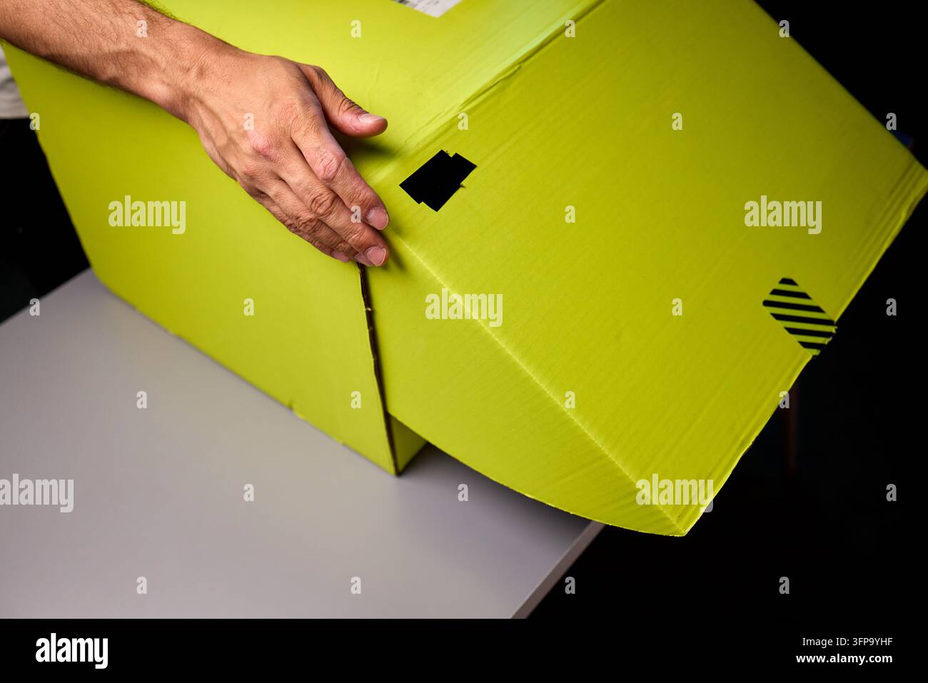 Hände, die eine hellgelbe Paketbox auf einer Tischplatte öffnen Stockfoto