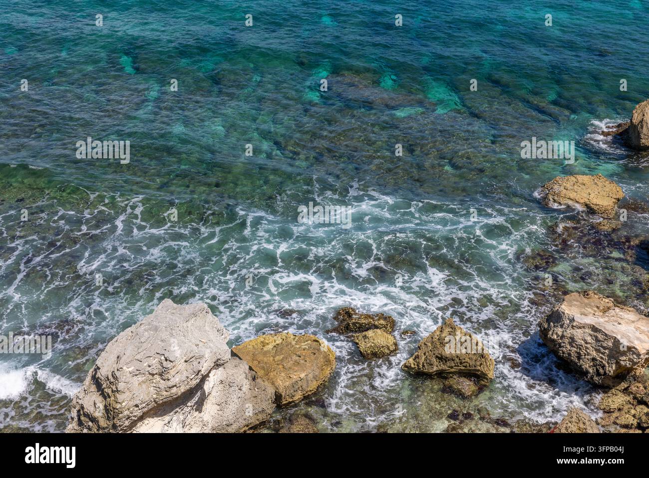 Luftaufnahme von klarem, türkisfarbenem Karibikwasser, das über eine felsige Küste schwappt, mit schaumigen Wellen und Kalksteinfelsen im Hintergrund Stockfoto