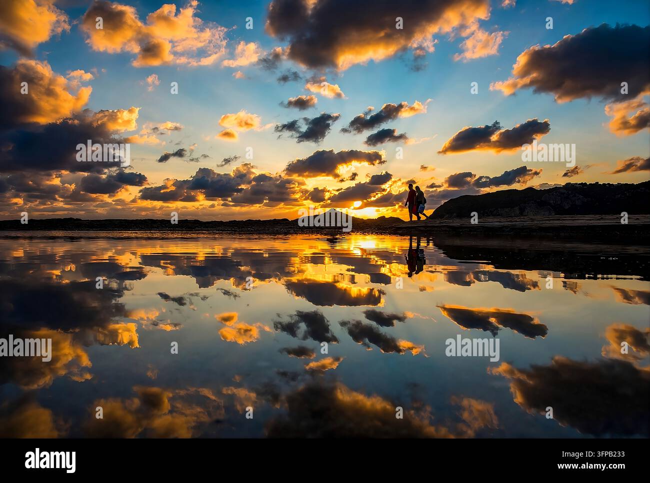 Dramatischer goldener Sonnenuntergang mit orangefarbenen Wolken, die sich im ruhigen Wasser des Agios-Georgios-Strandes auf Korfu, Griechenland, spiegeln, Silhouette eines gehenden Paares, Ionische Inseln Stockfoto