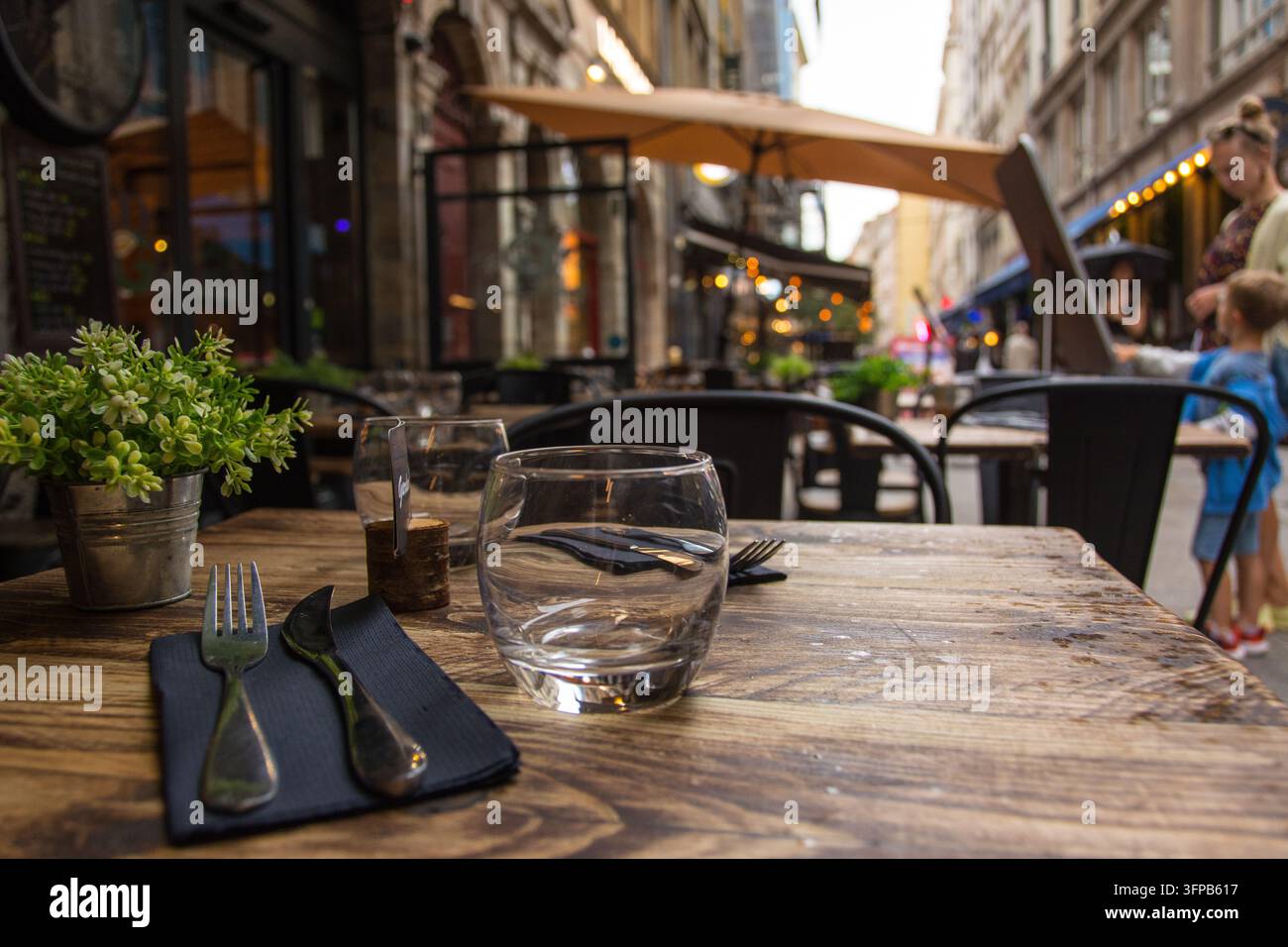 Terrasse eines Outdoor-Restaurants in einer historischen Straße von Lyon in der Dämmerung, mit einem schön gedeckten Tisch, der eine gemütliche Essatmosphäre schafft Stockfoto