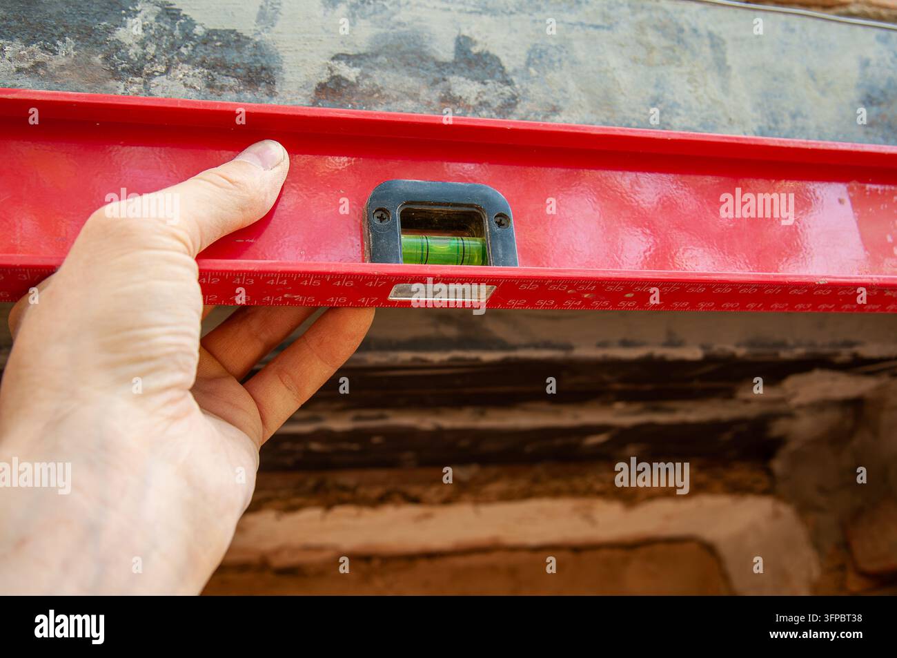 Eine Hand einer Person greift einen roten Wasserwaage-Level, um sicherzustellen, dass eine Oberfläche perfekt horizontal ist, wobei die Blase in der Kapsel zentriert ist Stockfoto