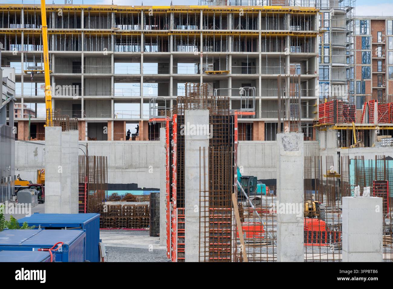 Eine geschäftige urbane Baustelle mit Arbeitern in einem unfertigen mehrstöckigen Betongebäude, umgeben von Stahlbetonsäulen Stockfoto