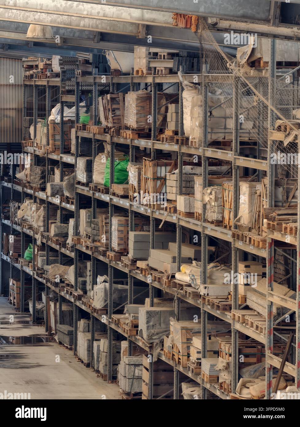 Hohe Lagerregale lagern verpackte Steinplatten, Holzkisten, Paletten und verpackte Materialien in einem geräumigen Industrie-Lagerbereich, wodurch org Stockfoto