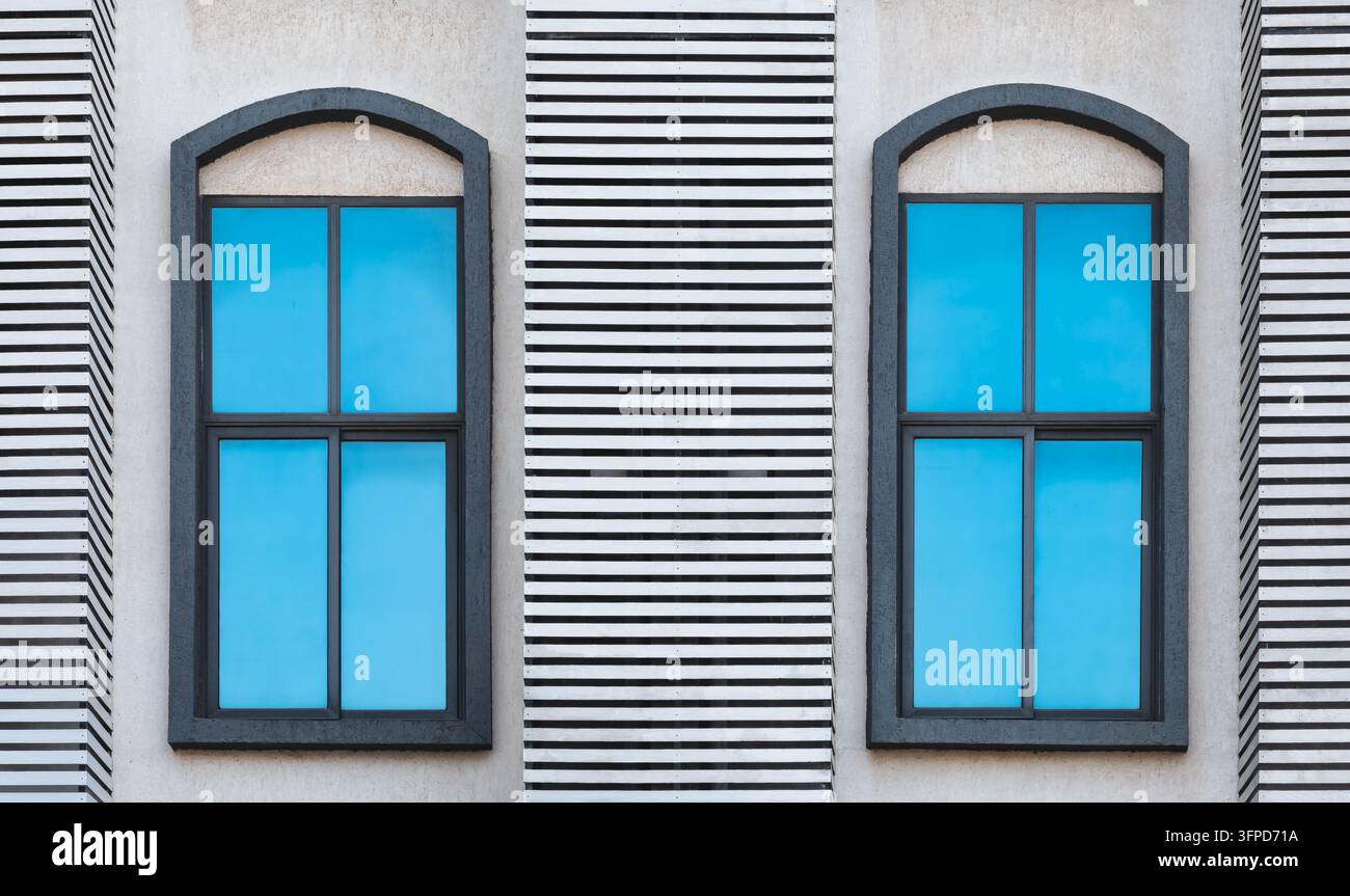 Fassade eines Hauses mit zwei großen Fenstern. Architektonisches Außendetail von zwei großen modernen Fenstern mit blau getönten Glasscheiben in einer Betonfassade Stockfoto