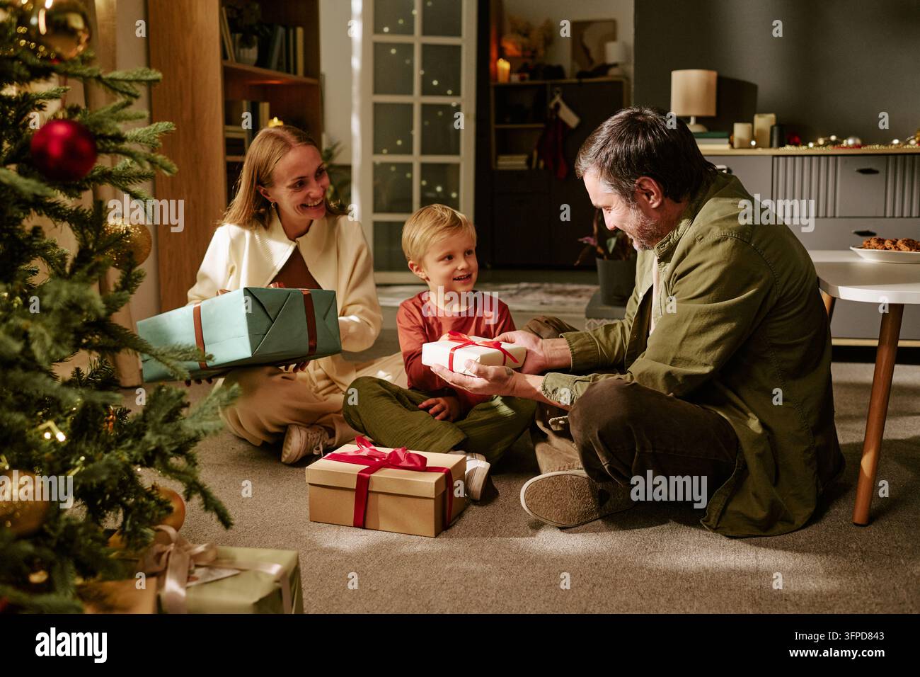Glückliche Familie mit Kind, das Geschenke am Weihnachtsbaum austauscht Stockfoto