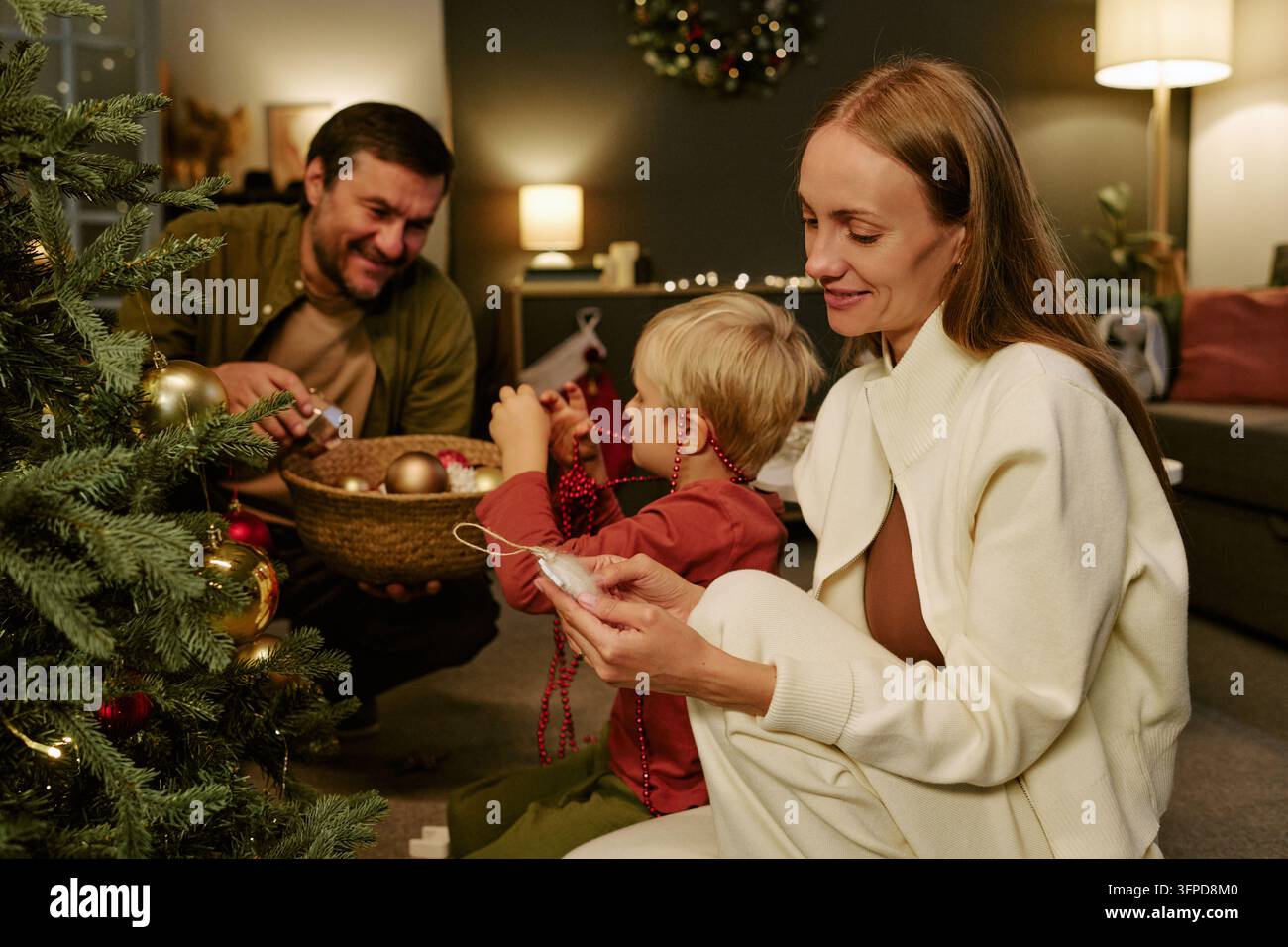 Glückliche Familie mit Kind schmückt den Weihnachtsbaum zu Hause Stockfoto