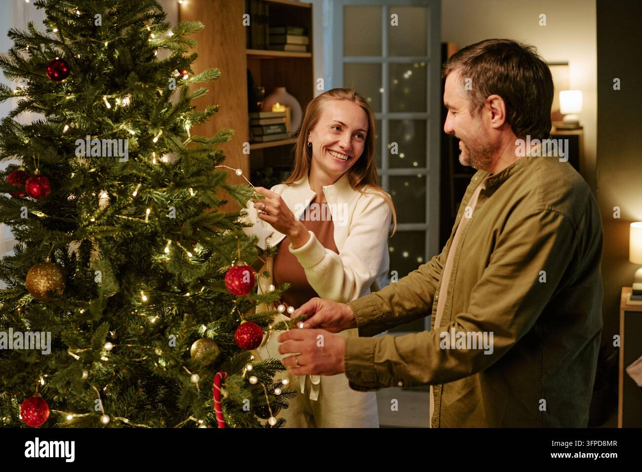 Glückliches Paar dekoriert den Weihnachtsbaum mit Lichtern zu Hause Stockfoto