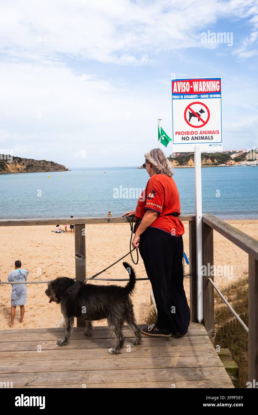 Hund und Frau stehen neben einem „Keine Tiere“-Schild am Strand von São Martinho do Porto, Portugal Stockfoto