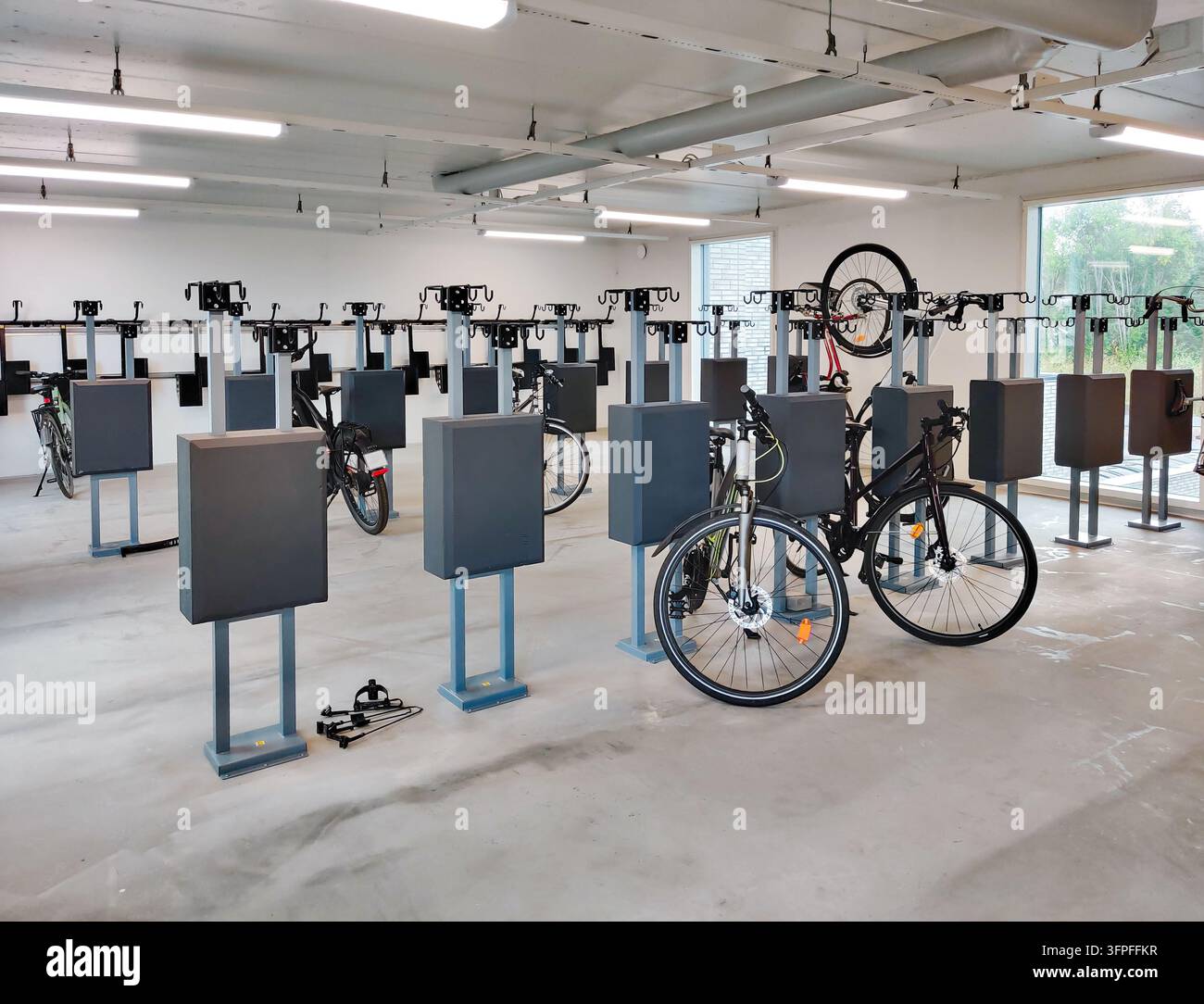 Eine indoor-Fahrradabstellanlage mit modernen vertikalen Parkständern und Ständern, mit mehreren abgestellten Fahrrädern und heller Deckenbeleuchtung Stockfoto