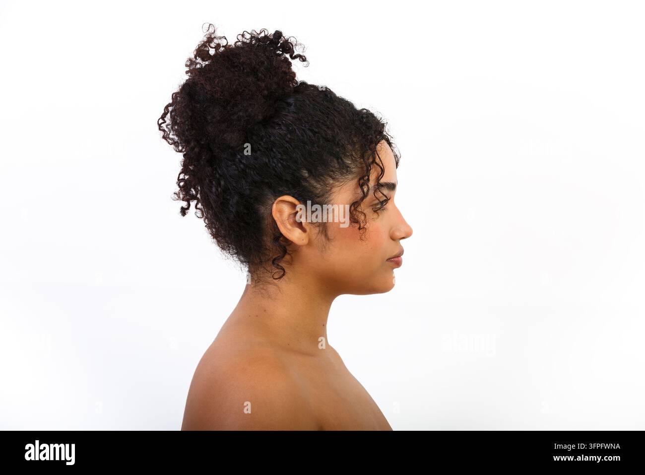 Eine Frau mit lockigem Haar wird im Profil gezeigt. Sie hat ein Interesse an Schönheit und Hautpflege. Der Hintergrund ist schlicht. Diese Szene hebt hervor Stockfoto