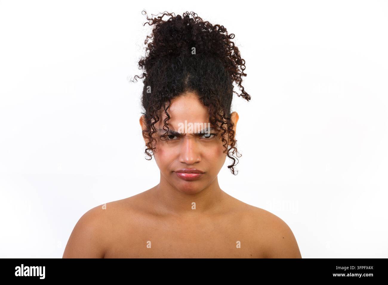 Eine hispanische Frau posiert mit ernstem Gesichtsausdruck und zeigt ihre Haut. Der Fokus liegt auf Gesundheits- und Schönheitspflege. Der Hintergrund ist weiß, was ihn betont Stockfoto