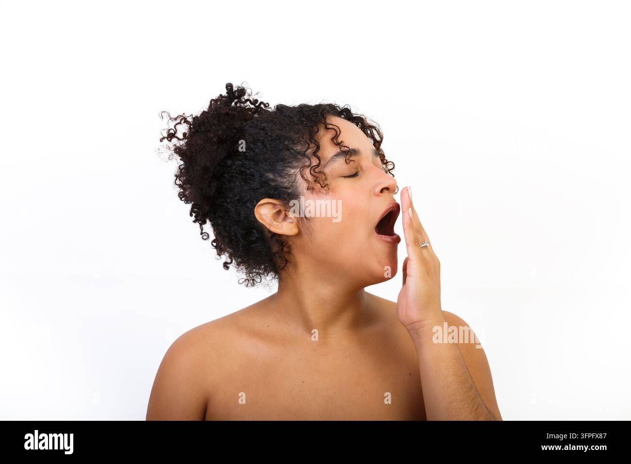 Eine hispanische Frau demonstriert Hautpflege-Bewusstsein in einer Studio-Umgebung. Sie gähnt und benutzt ihre Hand, um ihren Mund zu bedecken. Stockfoto