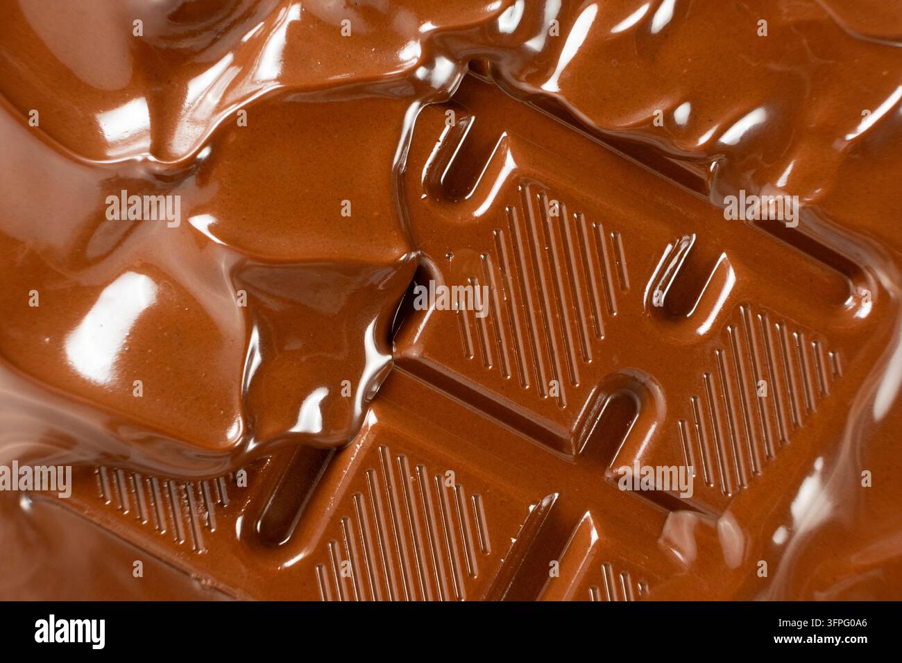 Schmelzender Schokoladenstrom, der über eine gerillte Schokoladenriegel fließt, Nahaufnahme. Stockfoto