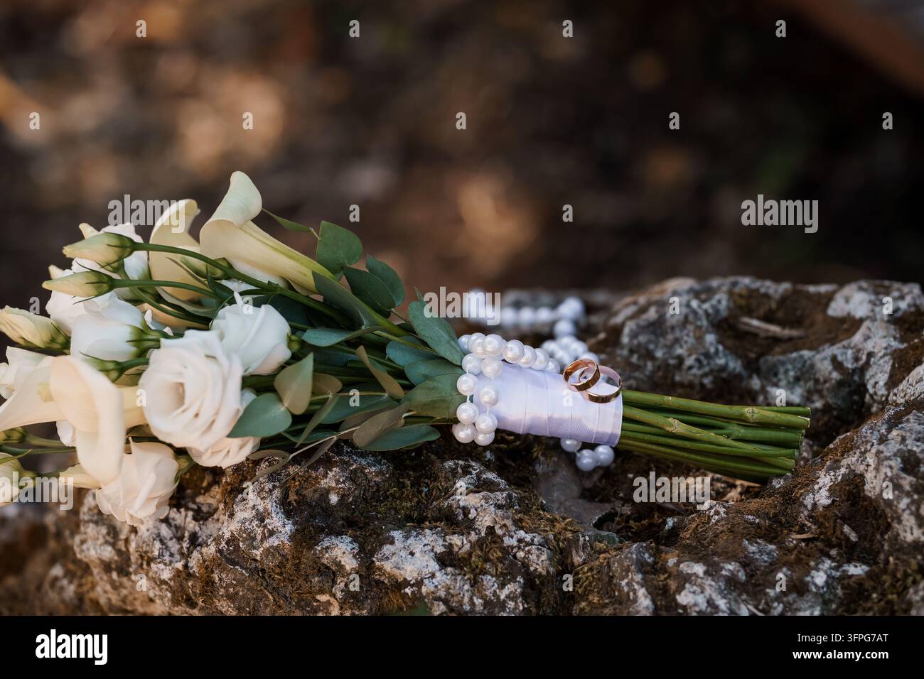 Elegante weiße Blumenkomposition gepaart mit passenden Eheringen und einer Perlenkette schafft ein romantisches zeremonielles Stillleben für Hochzeitsredaktion Stockfoto