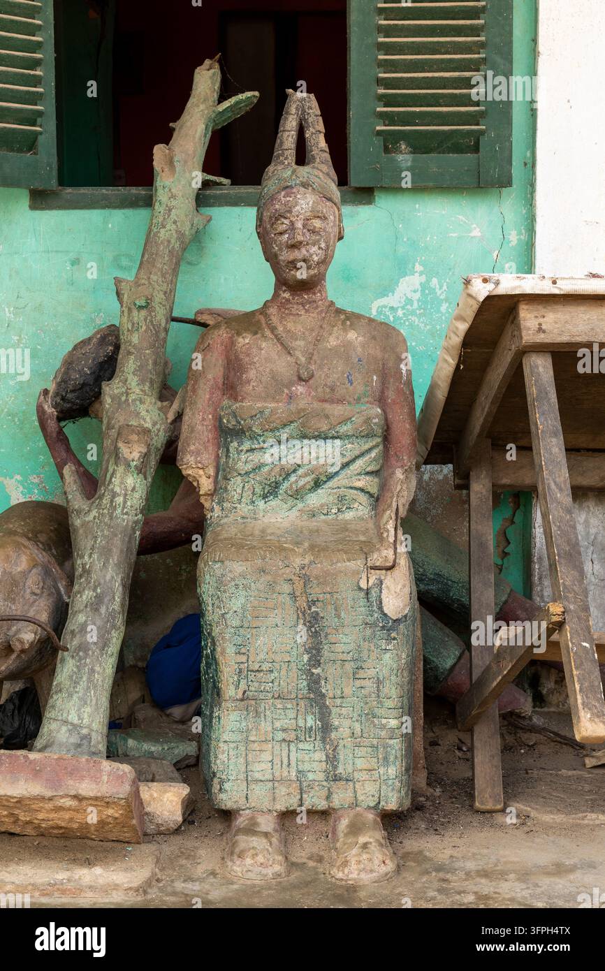 Verwitterte Betonstatue einer sitzenden Frau mit traditionellem Kopfschmuck vor einem Haus, Zentralregion, Elmina, Ghana Stockfoto