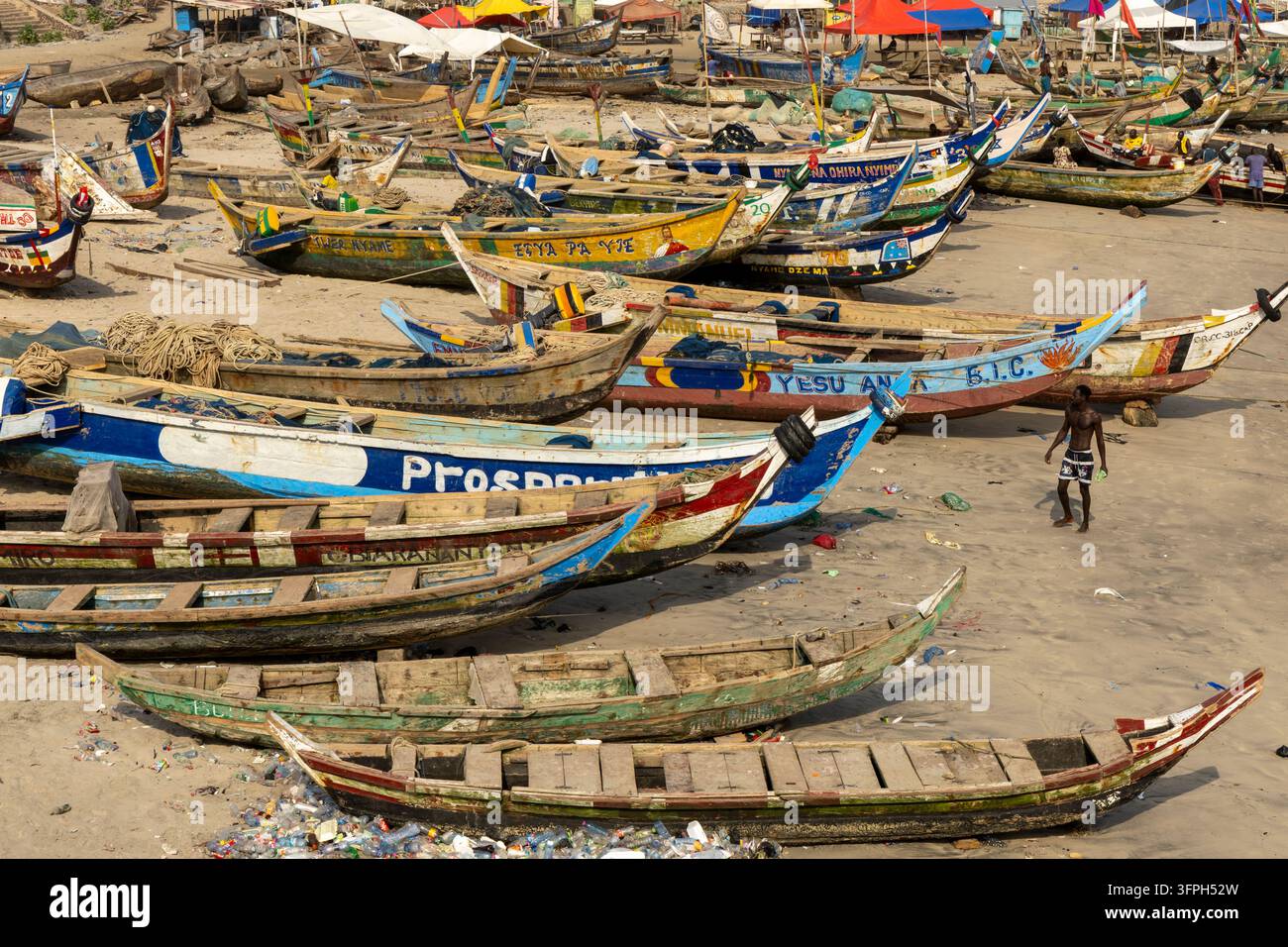 Reihen farbenfroher traditioneller Fischerboote, die am sandigen Strand aufgereiht sind, Zentralregion, Cape Coast, Ghana Stockfoto