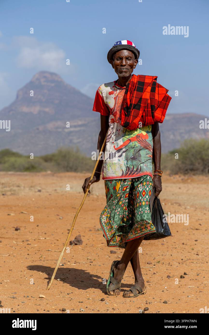 Älterer Mann des Samburu-Stammes in einem farbenfrohen Hemd und rotem kariertem Shuka, gestützt auf einen Gehstock, Samburu County, Samburu, Kenia Stockfoto