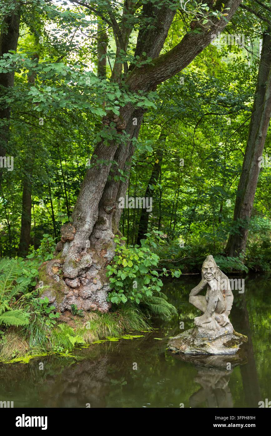 Steinstatue eines Goblins, die auf einem Felsen in einem Teich hockt, umgeben von grünem Waldlaub Stockfoto